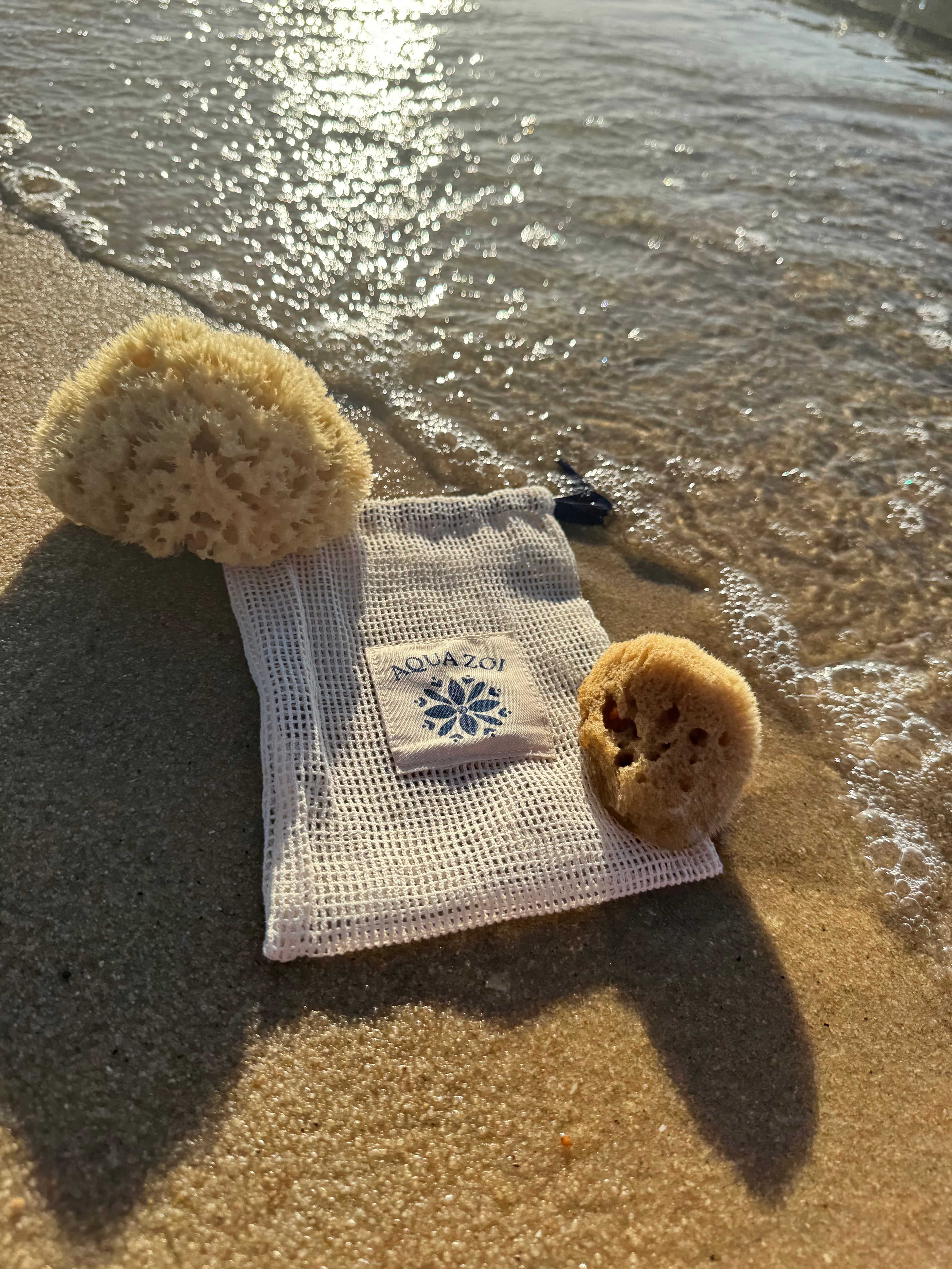 Mesh bag with Aqua Zoi logo on a sandy beach with sea sponges around