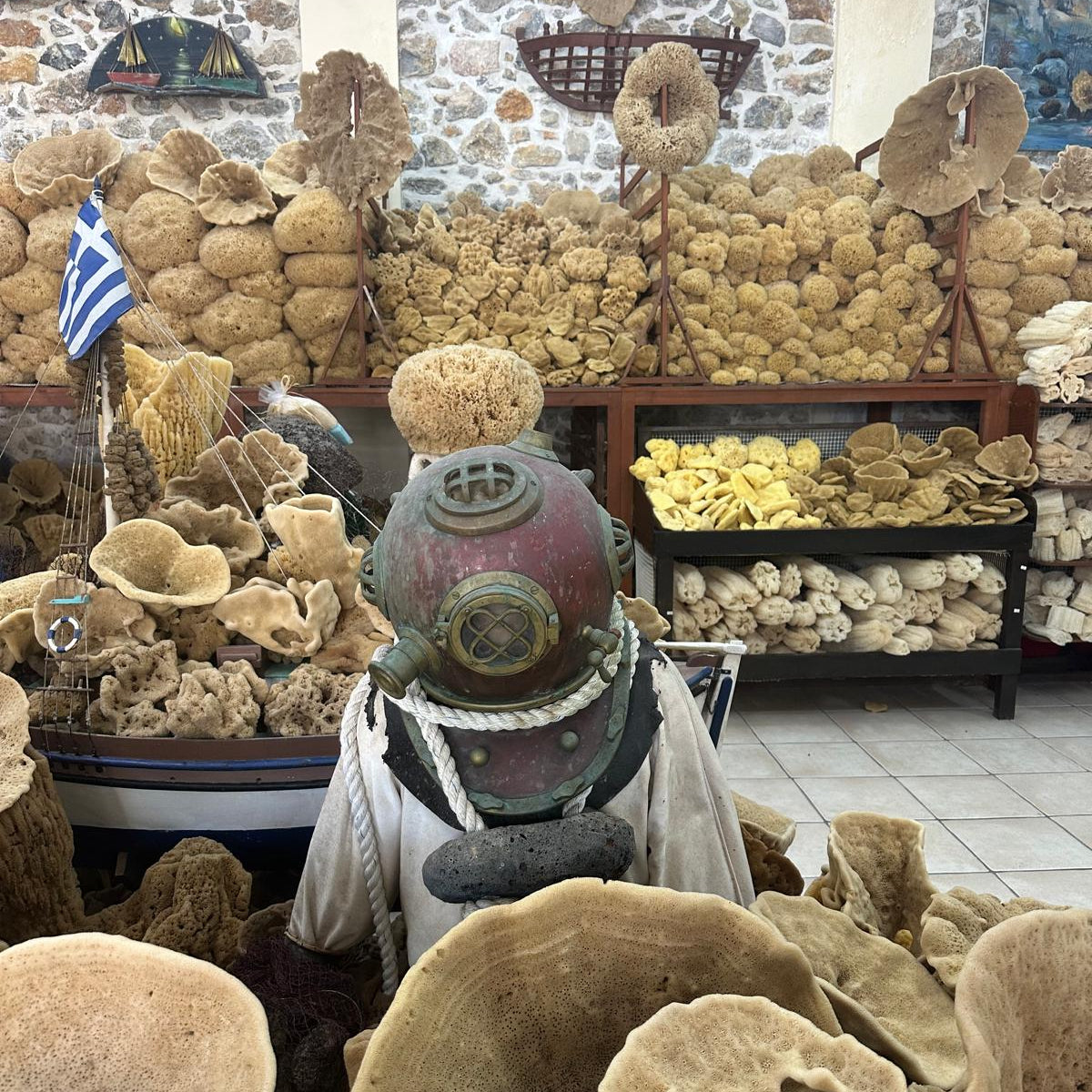 Display of various sponges with a diving helmet and small boat in a store setting.