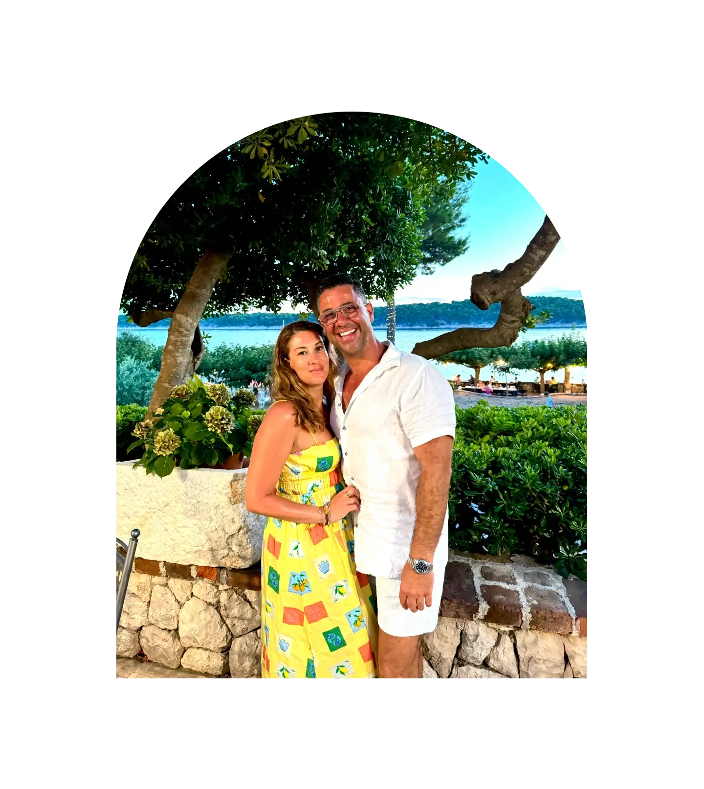 Couple standing together in a scenic outdoor setting with trees and water in the background.