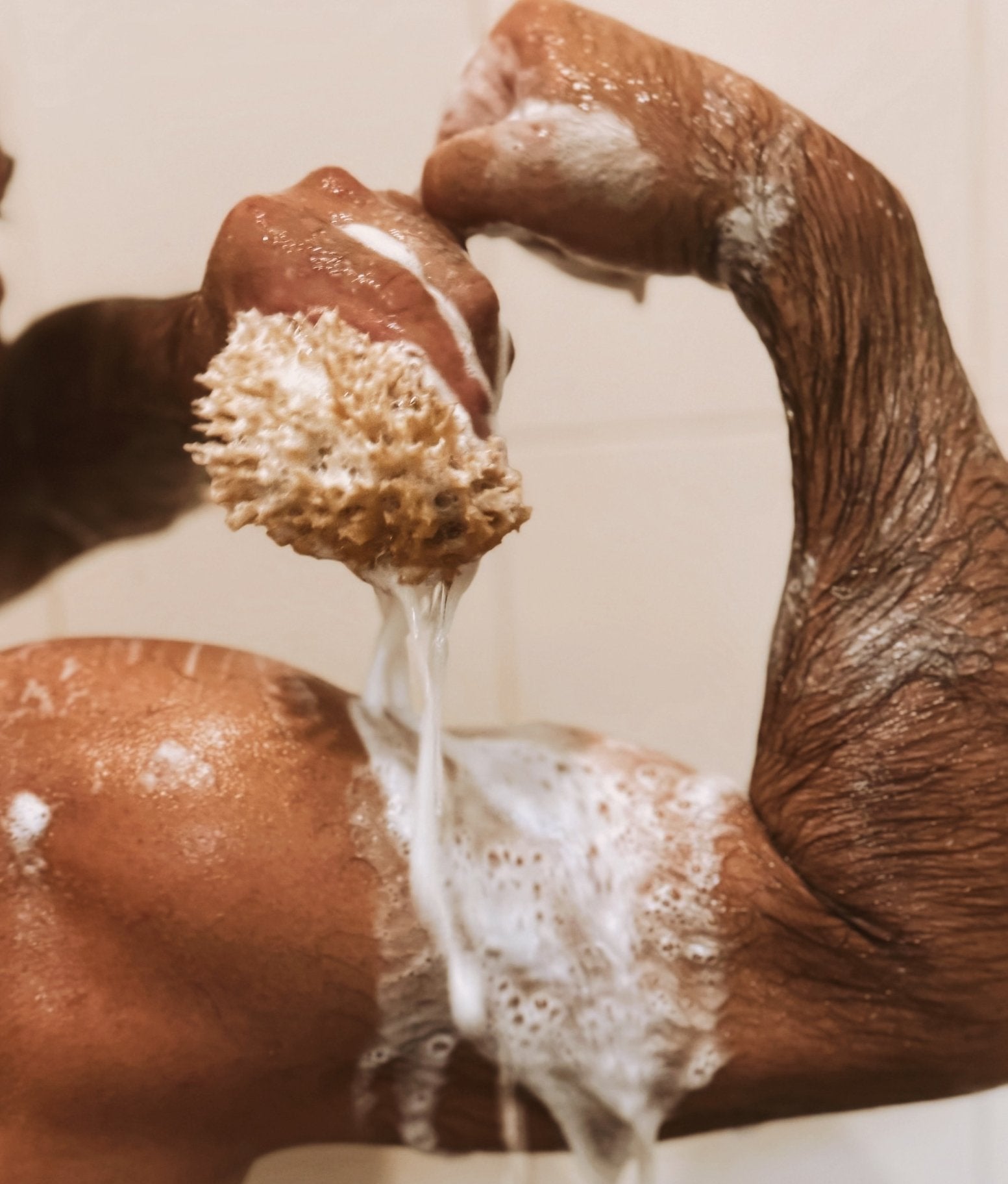 Close-up of a person scrubbing their arm with a natural sea sponge in the shower