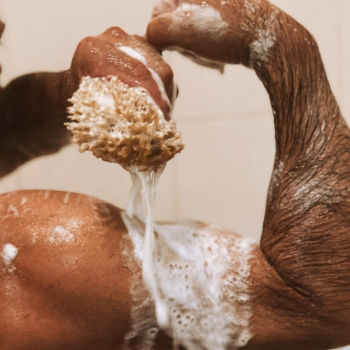 Close-up of a person scrubbing their arm with a natural sea sponge in the shower