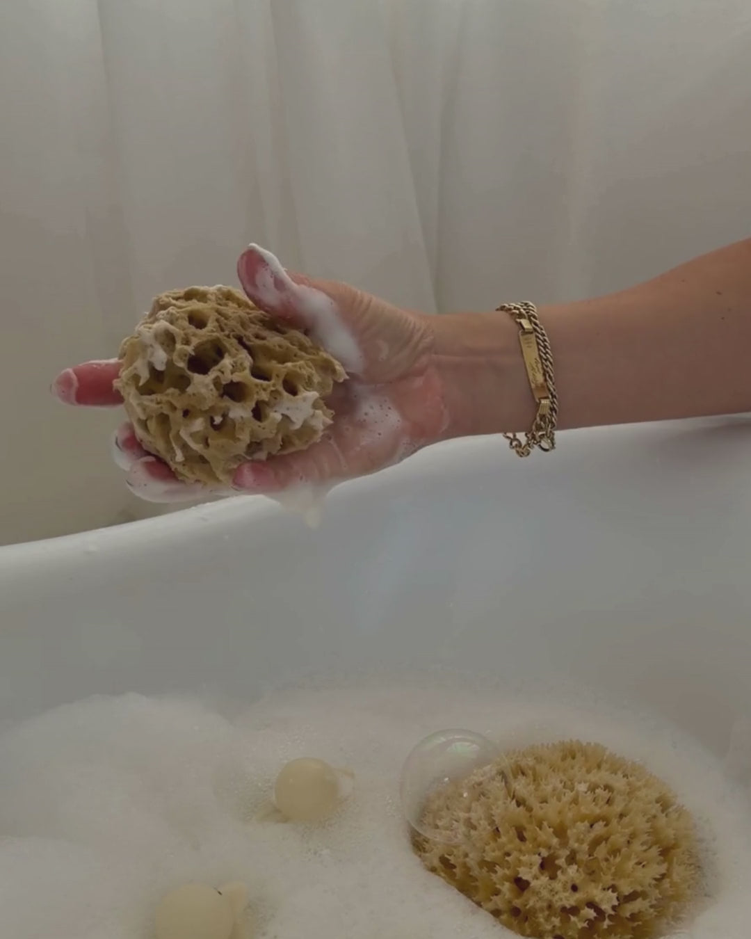 natural sea sponge in hand with lather over baby bath