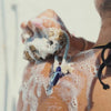 model washing her shoulder with natural sea sponge with cream cord and mati glass charm showing lather 
